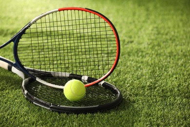 Photo of Tennis rackets and ball on green artificial grass, closeup. Space for text