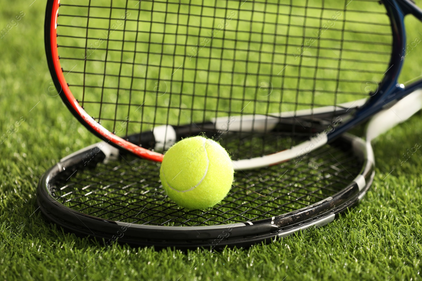 Photo of Tennis rackets and ball on green artificial grass, closeup