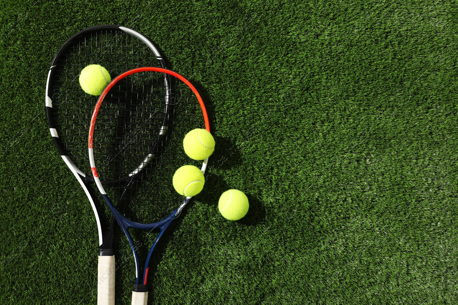 Photo of Tennis rackets and balls on green artificial grass, flat lay. Space for text