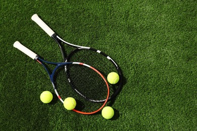 Photo of Tennis rackets and balls on green artificial grass, flat lay. Space for text