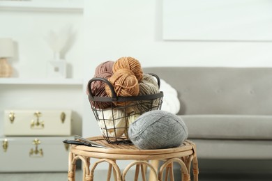 Photo of Skeins of soft yarn, knitting needles and scissors on table indoors