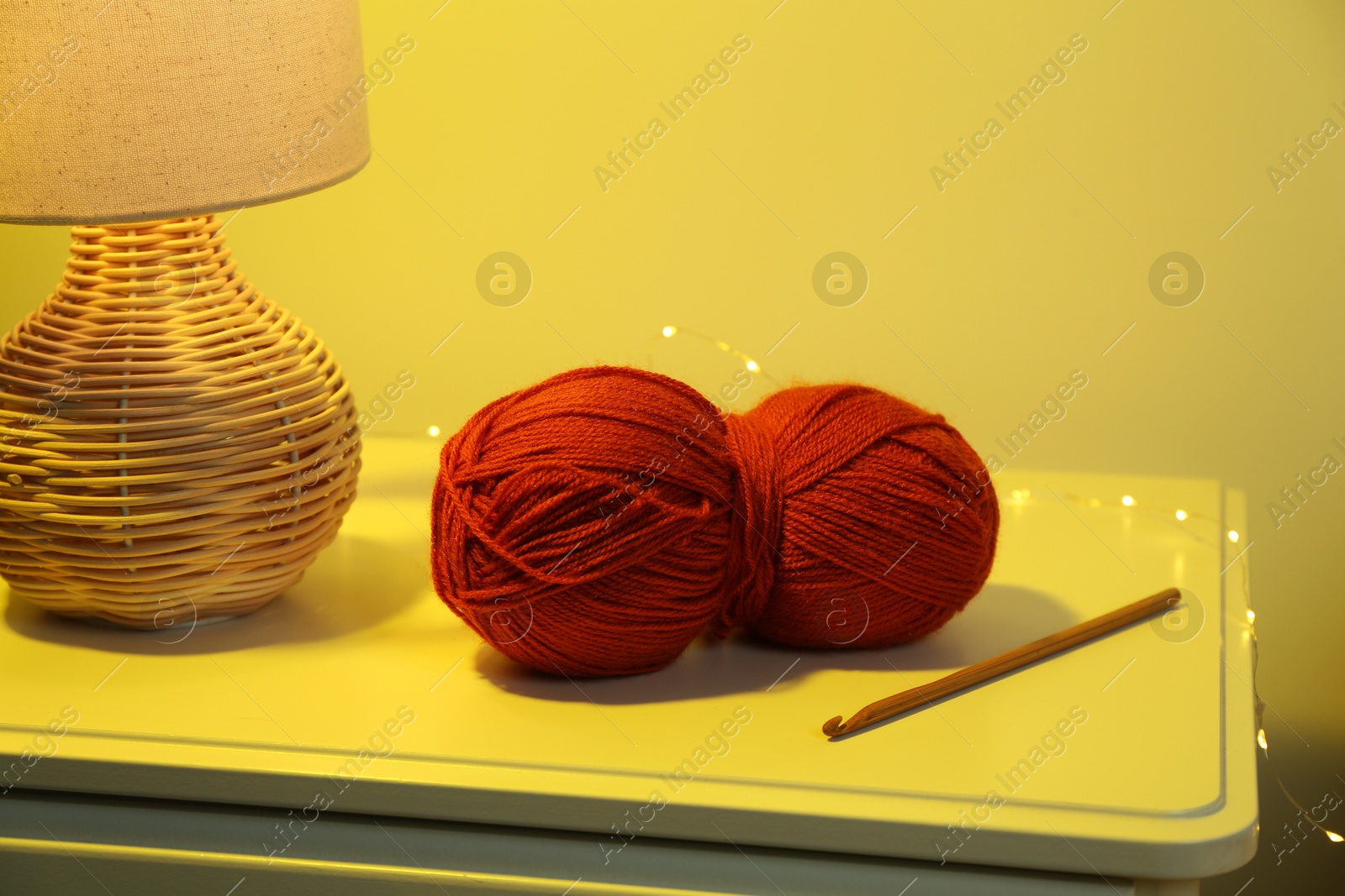 Photo of Knitting material. Skein of soft yarn, crochet hook and lamp on table indoors