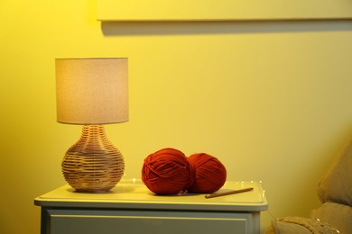 Photo of Knitting material. Skein of soft yarn, crochet hook and lamp on bedside table indoors