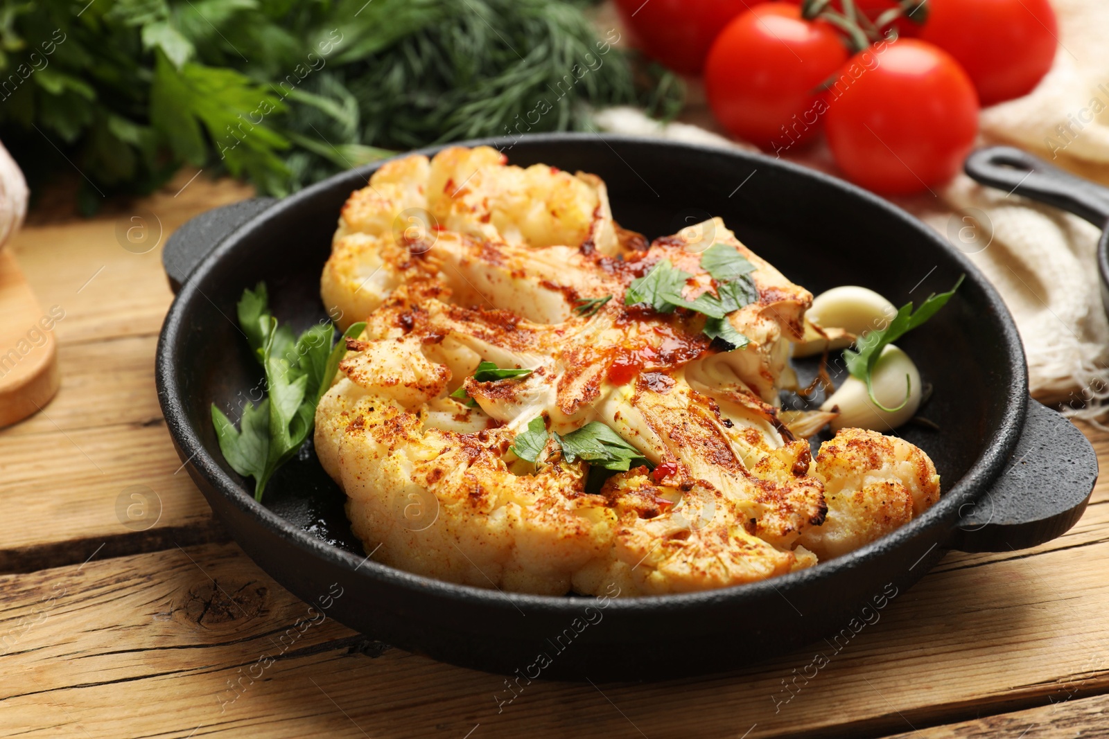 Photo of Tasty cauliflower steak in frying pan and other products on wooden table, closeup