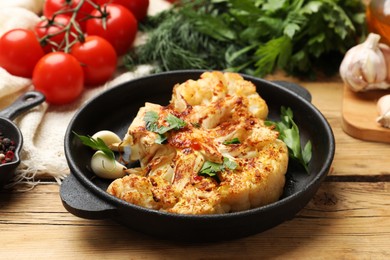 Photo of Tasty cauliflower steak in frying pan and other products on wooden table, closeup