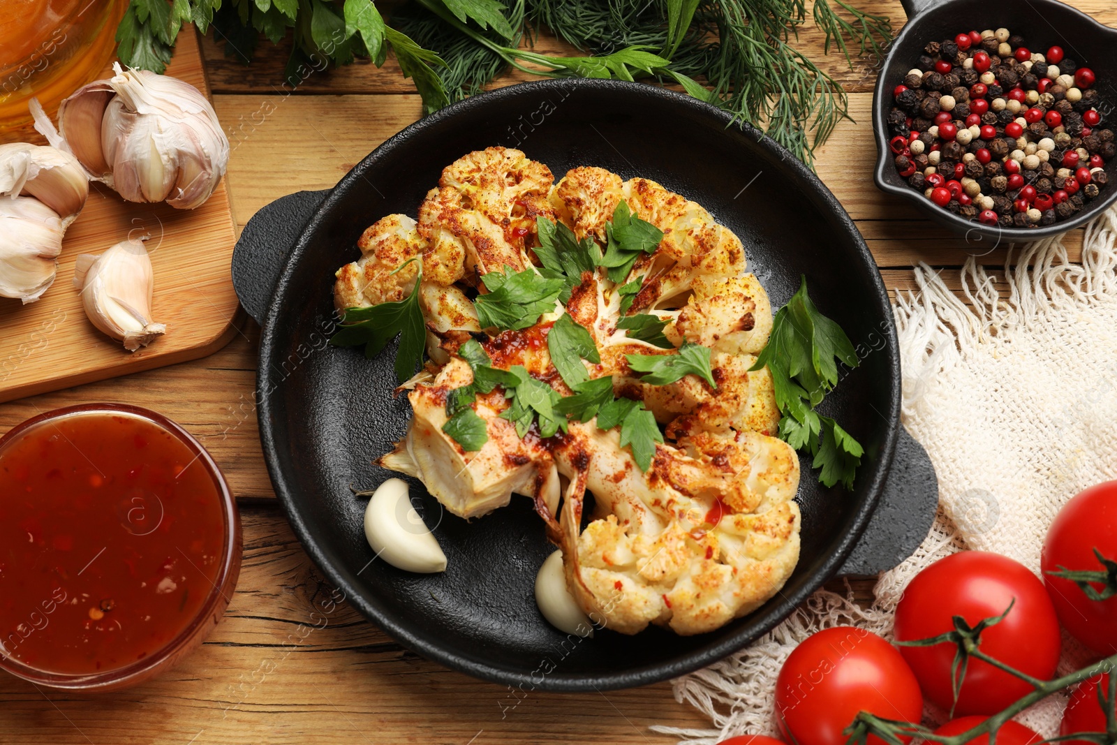 Photo of Tasty cauliflower steak in frying pan and other products on wooden table, top view