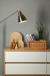 Photo of Different decorative elements on chest of drawers and lamp near gray wall indoors