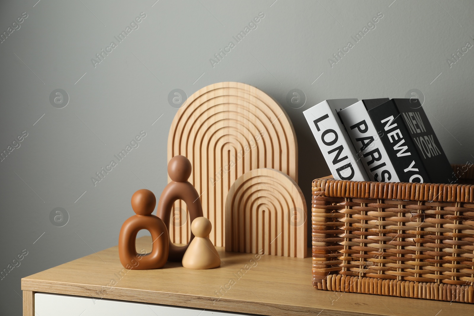 Photo of Different decorative elements and hardcover books with city names on chest of drawers near gray wall indoors