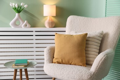 Photo of Two soft pillows on light armchair and side table with books in living room