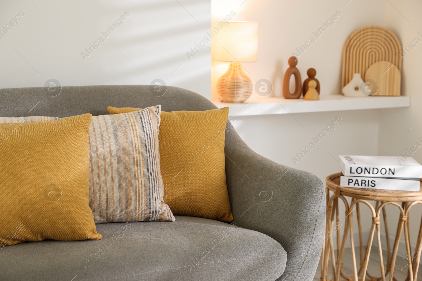 Photo of Different soft pillows on gray sofa and side table with books in living room