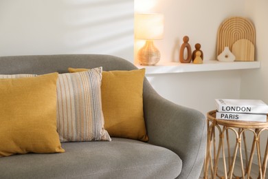 Photo of Different soft pillows on gray sofa and side table with books in living room