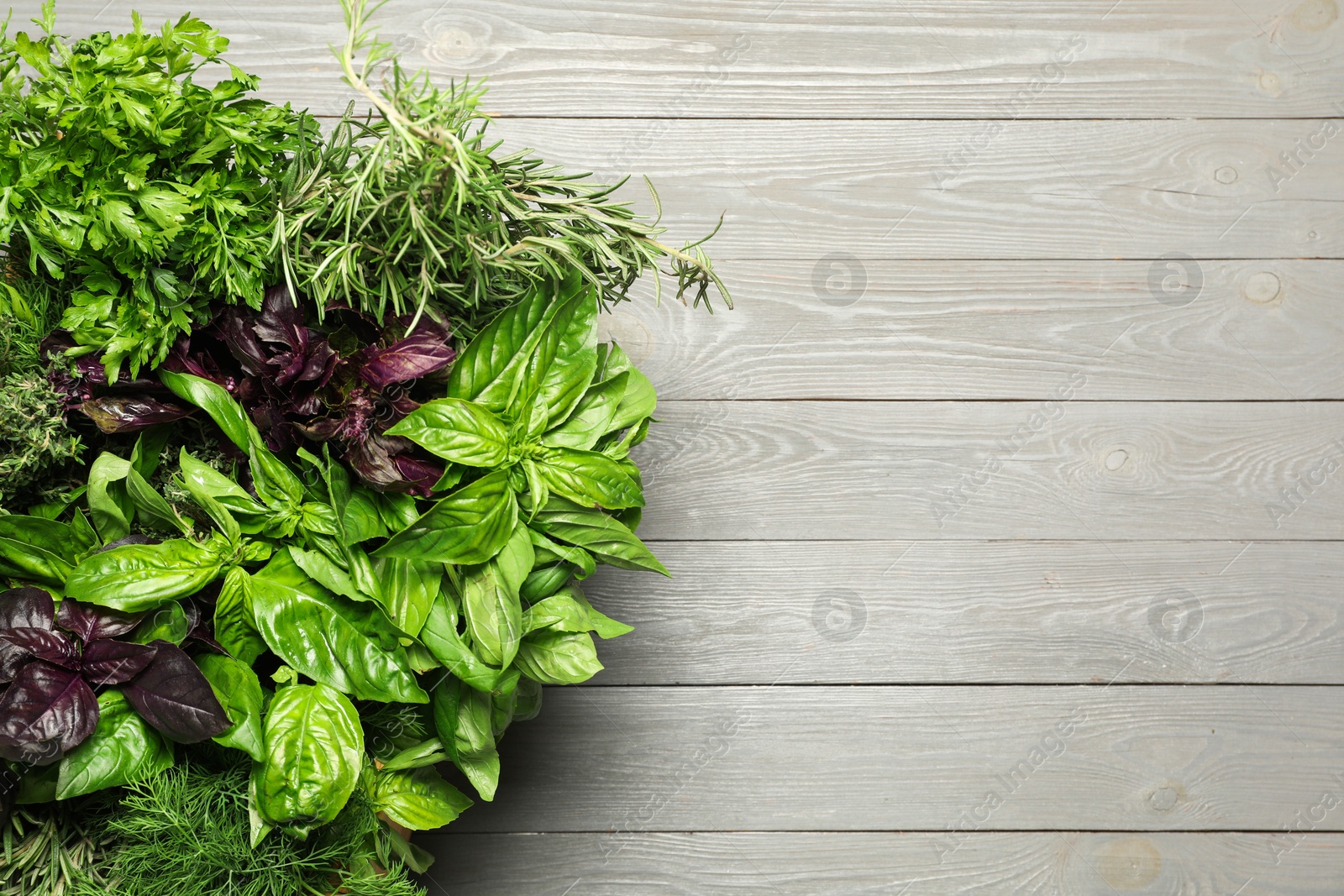 Photo of Different fresh herbs in basket on light grey wooden table, top view. Space for text