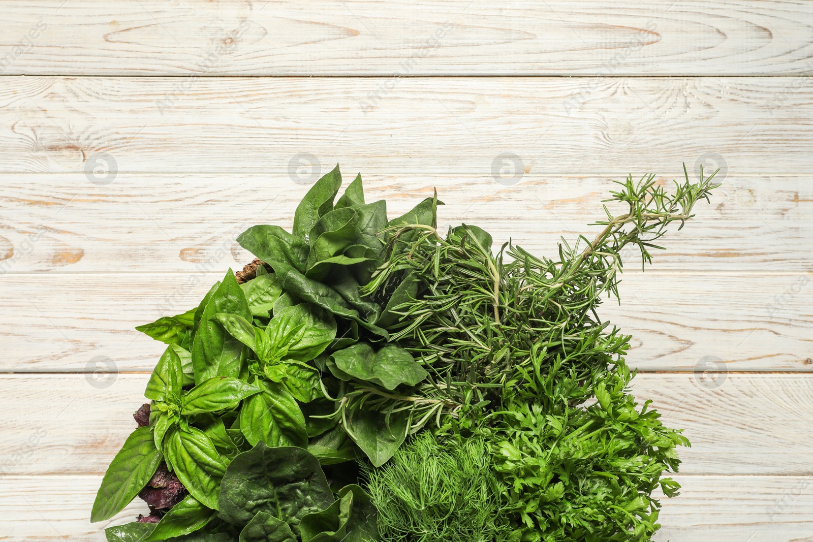 Photo of Different fresh herbs in basket on white wooden table, top view. Space for text