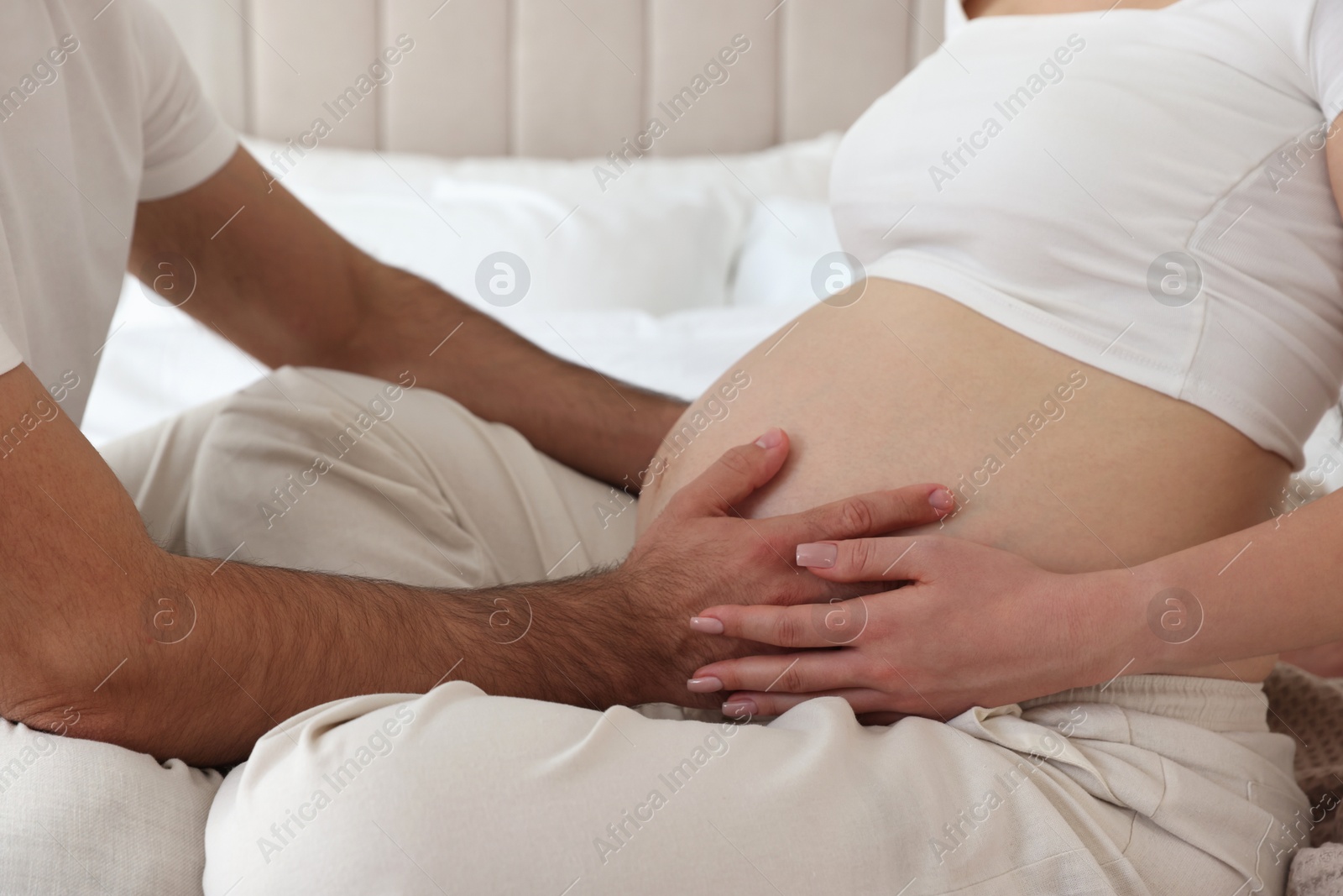 Photo of Man touching his pregnant wife's belly indoors, closeup