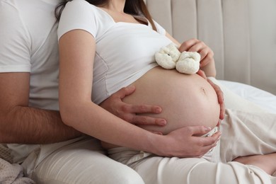 Pregnant woman with baby booties and her husband indoors, closeup