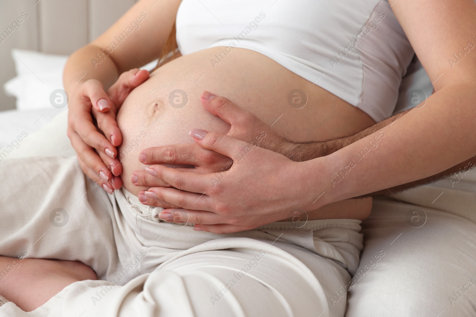 Photo of Man touching his pregnant wife's belly indoors, closeup