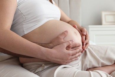 Photo of Man touching his pregnant wife's belly indoors, closeup