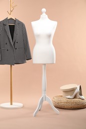 One female mannequin, pouf, shoes and rack with jacket against beige background