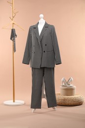 Female mannequin with suit, pouf, shoes and rack on beige background