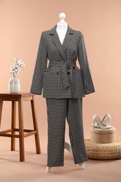 Photo of Female mannequin with suit, stool, cotton flowers, pouf and shoes on beige background