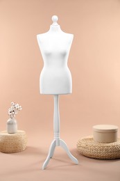 Female mannequin, poufs, box and vase with cotton flowers on beige background