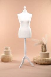 Photo of Female mannequin, poufs, boxes and vase with decorative plants on beige background