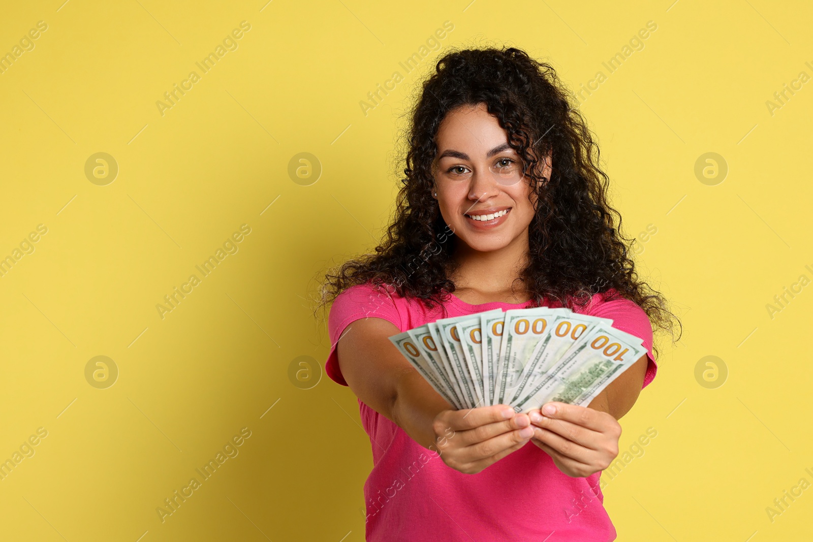 Photo of Happy woman with dollar banknotes on yellow background, space for text