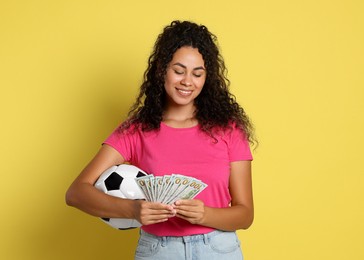 Happy woman with money and soccer ball on yellow background