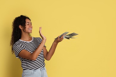 Happy woman throwing money on yellow background, space for text