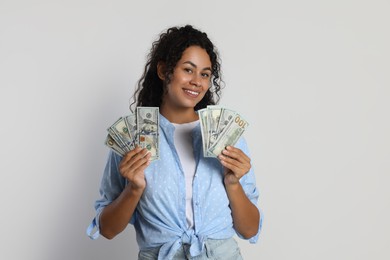 Happy woman with dollar banknotes on light grey background