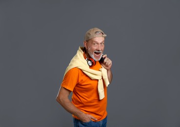 Portrait of emotional senior man with headphones on grey background