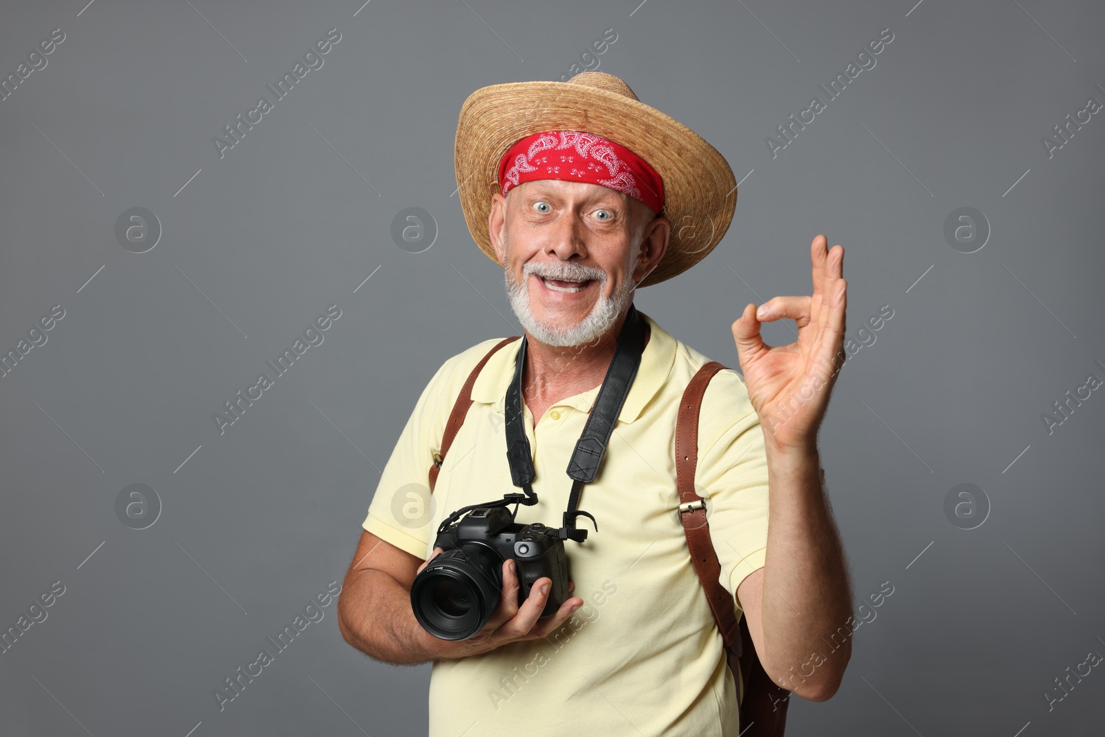 Photo of Portrait of happy senior man with camera showing ok gesture on grey background. Space for text