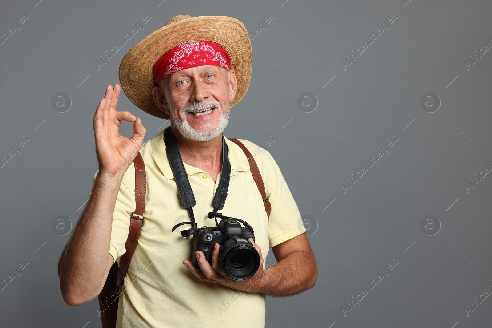 Photo of Portrait of happy senior man with camera showing ok gesture on grey background. Space for text