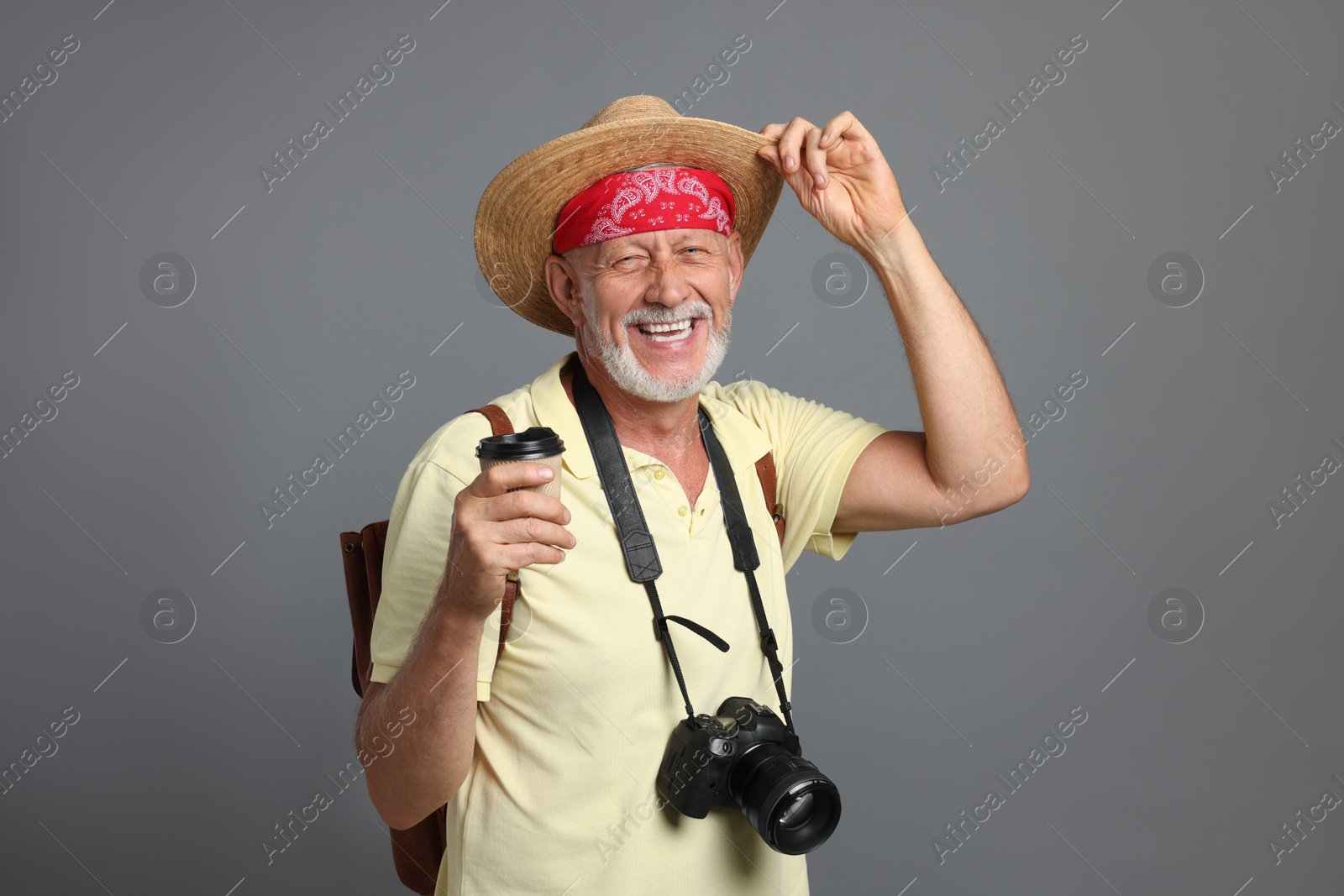 Photo of Portrait of happy senior man with camera and paper cup on grey background