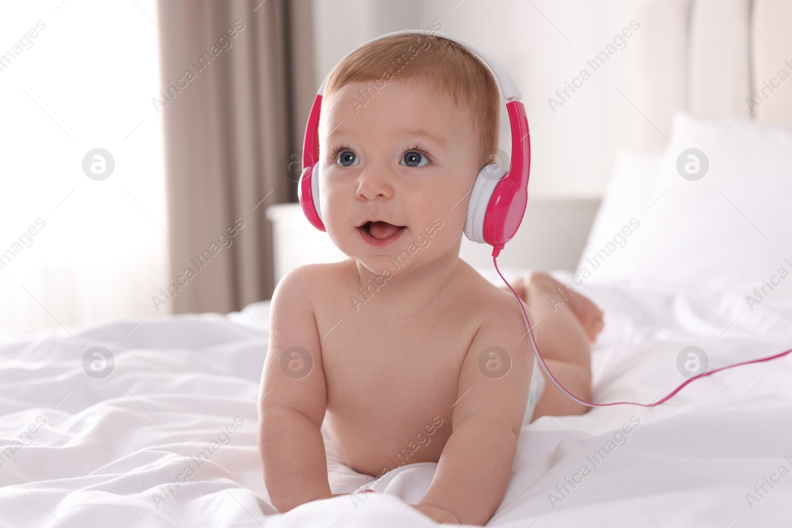 Photo of Cute little baby with headphones on bed at home