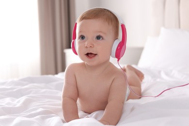 Cute little baby with headphones on bed at home