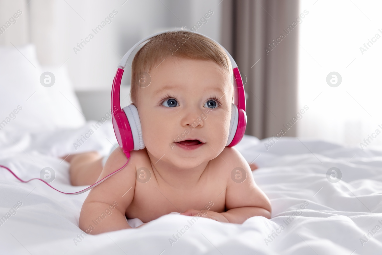 Photo of Cute little baby with headphones on bed at home