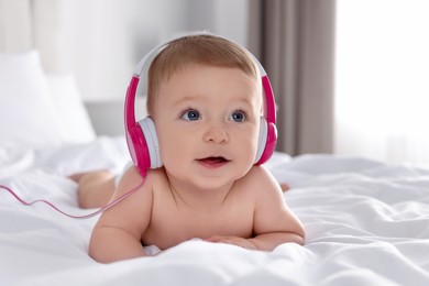 Photo of Cute little baby with headphones on bed at home