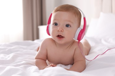 Cute little baby with headphones on bed at home