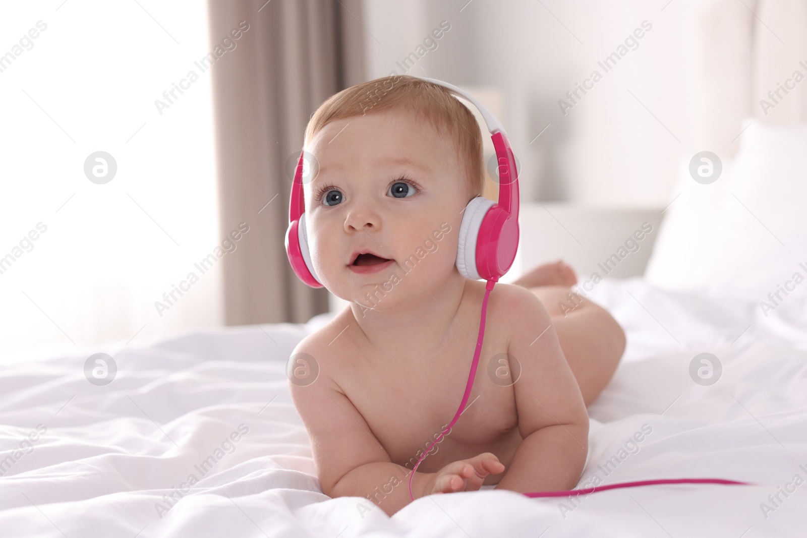 Photo of Cute little baby with headphones on bed at home