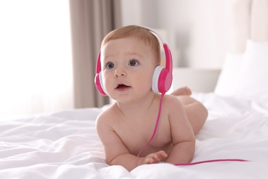 Photo of Cute little baby with headphones on bed at home