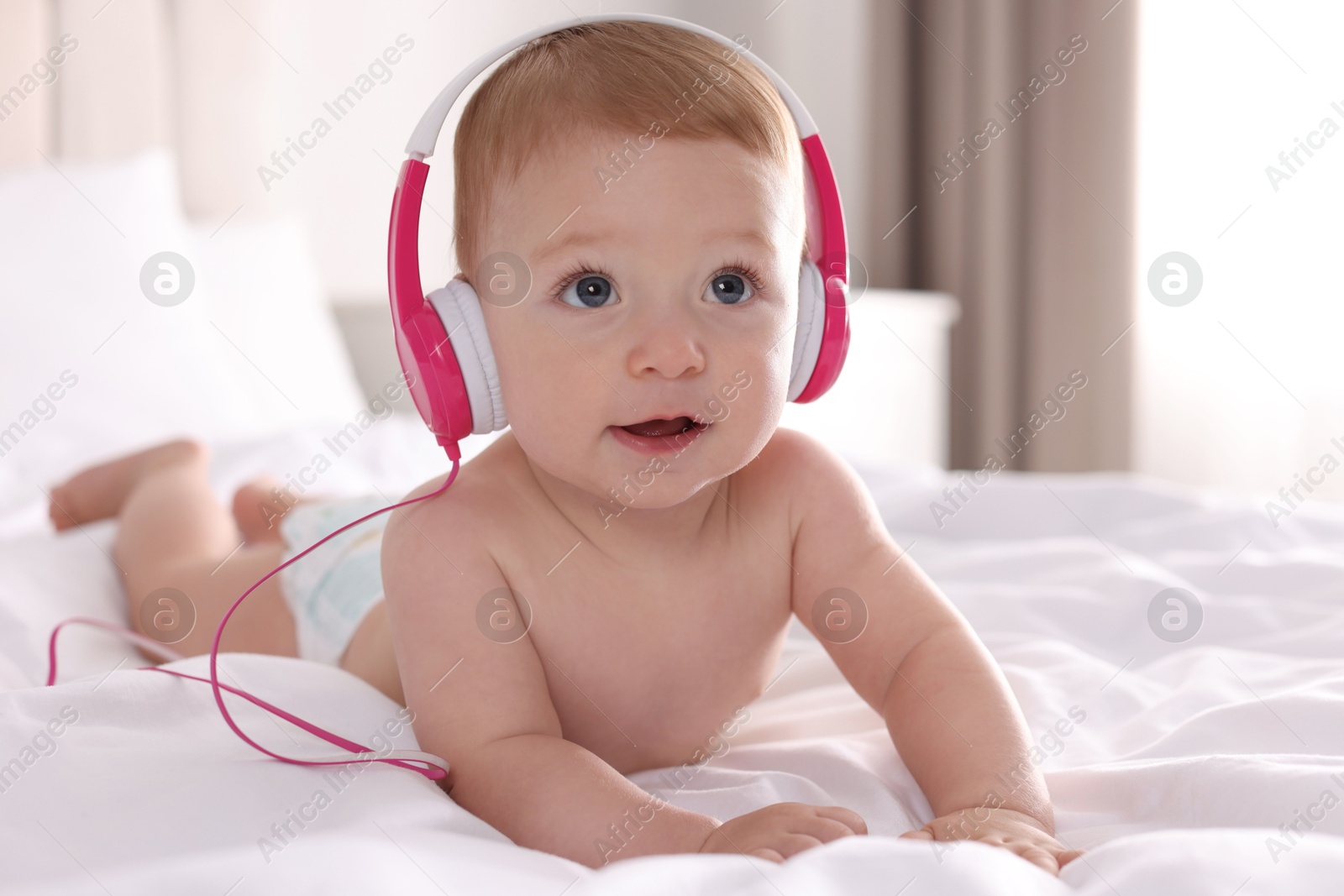 Photo of Cute little baby with headphones on bed at home