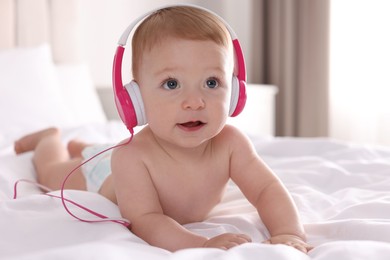 Cute little baby with headphones on bed at home