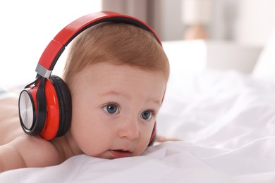 Cute little baby with headphones on bed at home, space for text