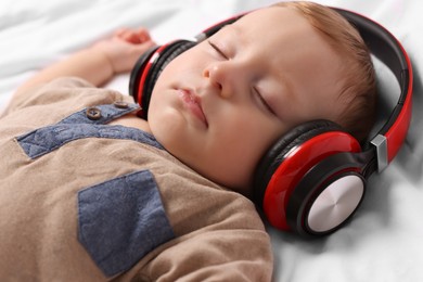 Cute little baby with headphones sleeping on bed