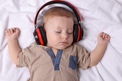 Photo of Cute little baby with headphones sleeping on bed, top view