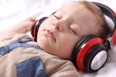 Cute little baby with headphones sleeping on bed