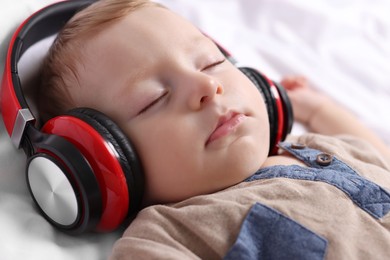 Photo of Cute little baby with headphones sleeping on bed