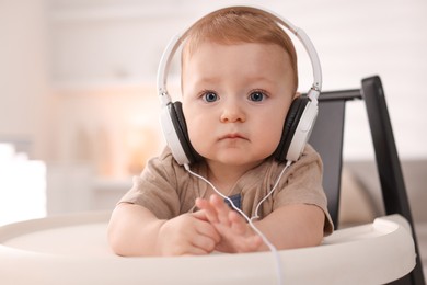 Photo of Cute little baby with headphones on high chair at home