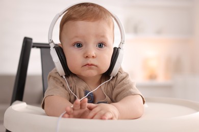 Photo of Cute little baby with headphones on high chair at home